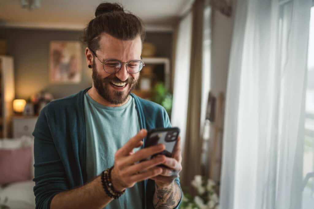 One adult caucasian man with eyeglasses beard, tattoos and hair write message or browse internet at home happy